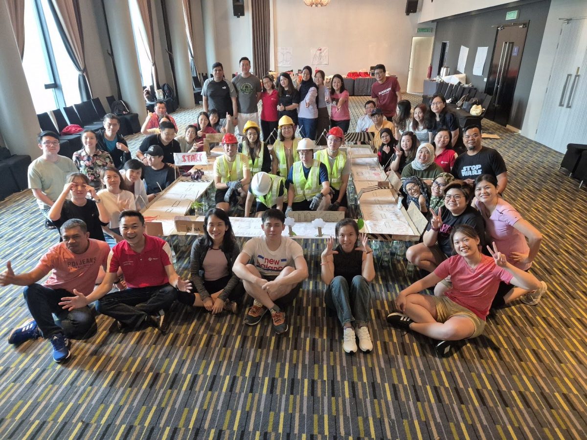 Large group photo of participants wearing hard hats and safety vests at a team building event