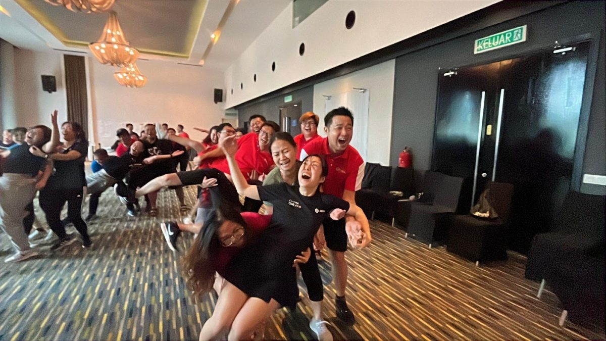 Team members forming a human wave during a team building activity in a ballroom